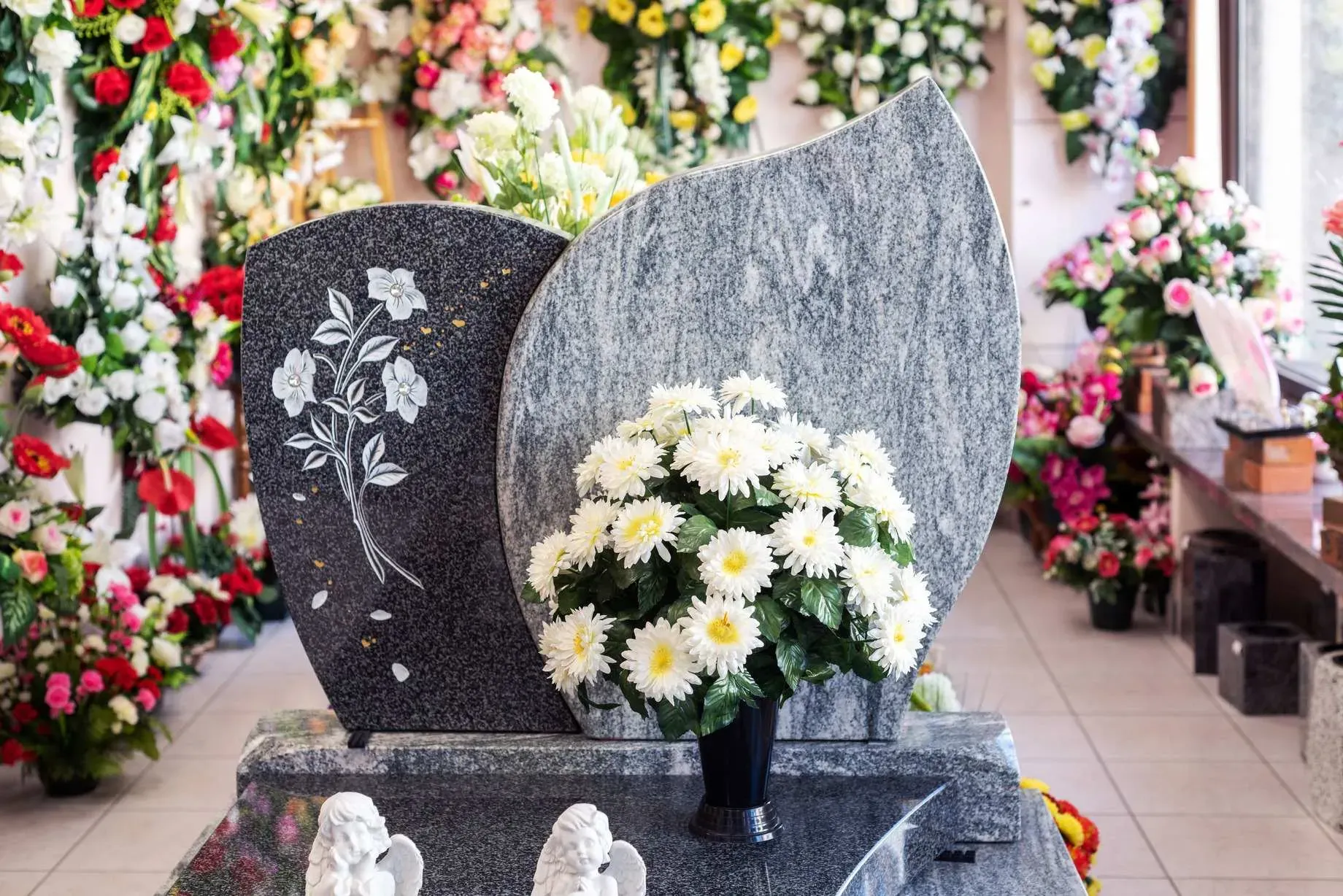 Stèle en granit gravée avec vase de fleurs blanches et anges en résine.