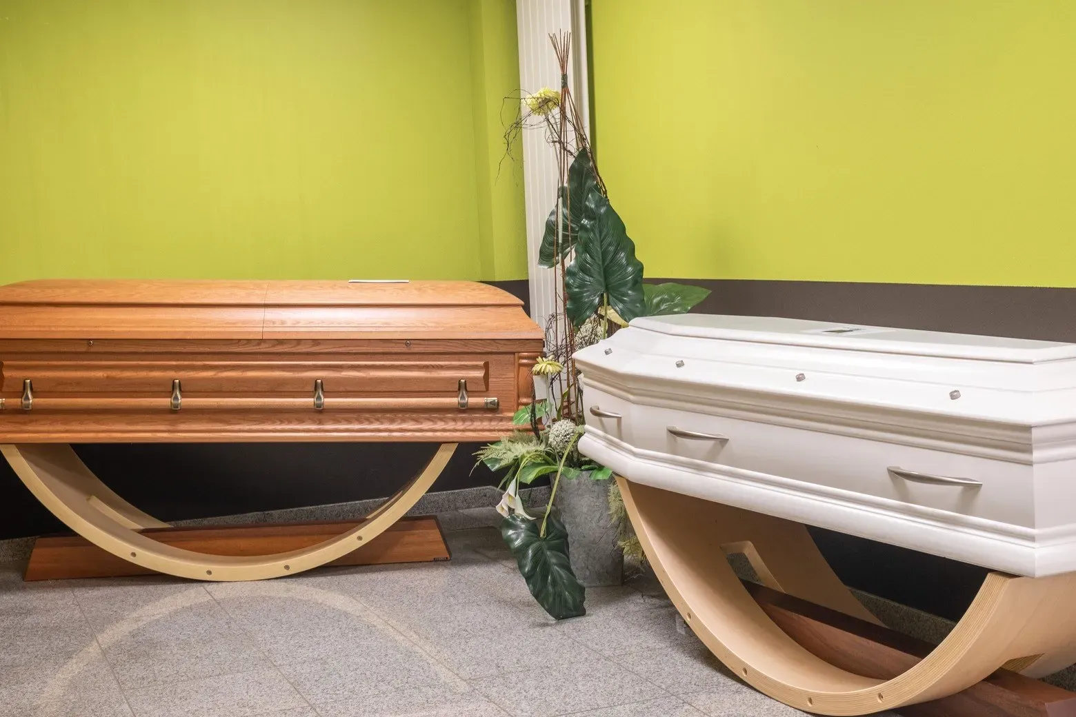 Gros plan sur deux cercueils exposés, un en bois clair poli et un blanc.