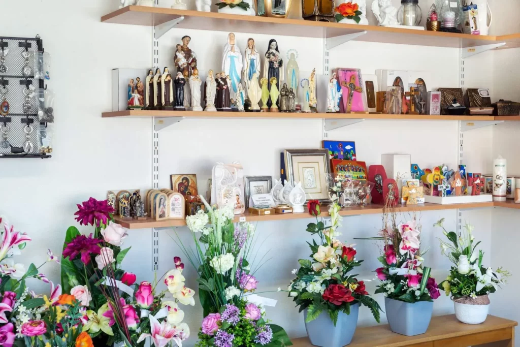 Rayonnage d'articles religieux, statuettes et compositions florales en boutique.